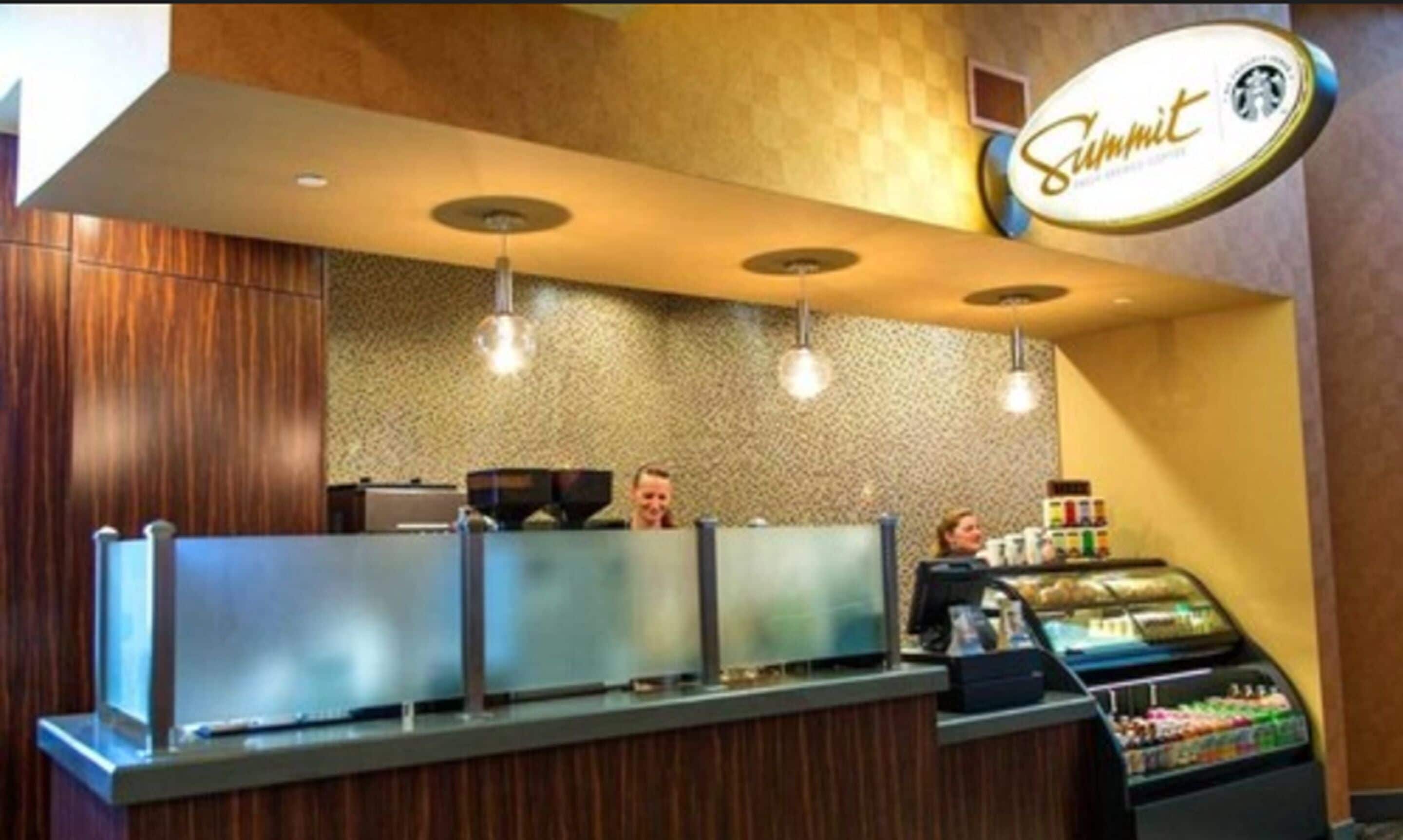 A coffee shop counter with a branded sign, a cash register, and a refrigerated display case.