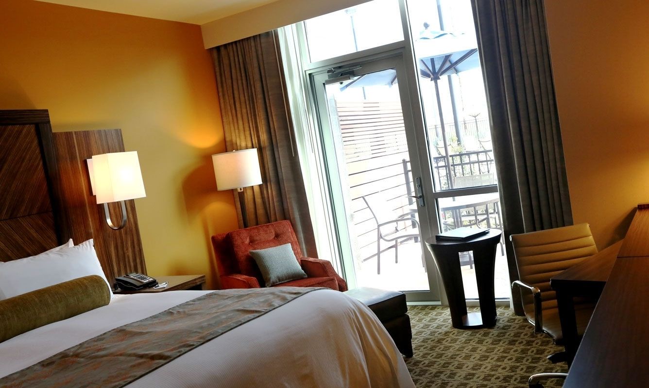 A hotel room with a large bed, two chairs, a small table, and a balcony with a railing.