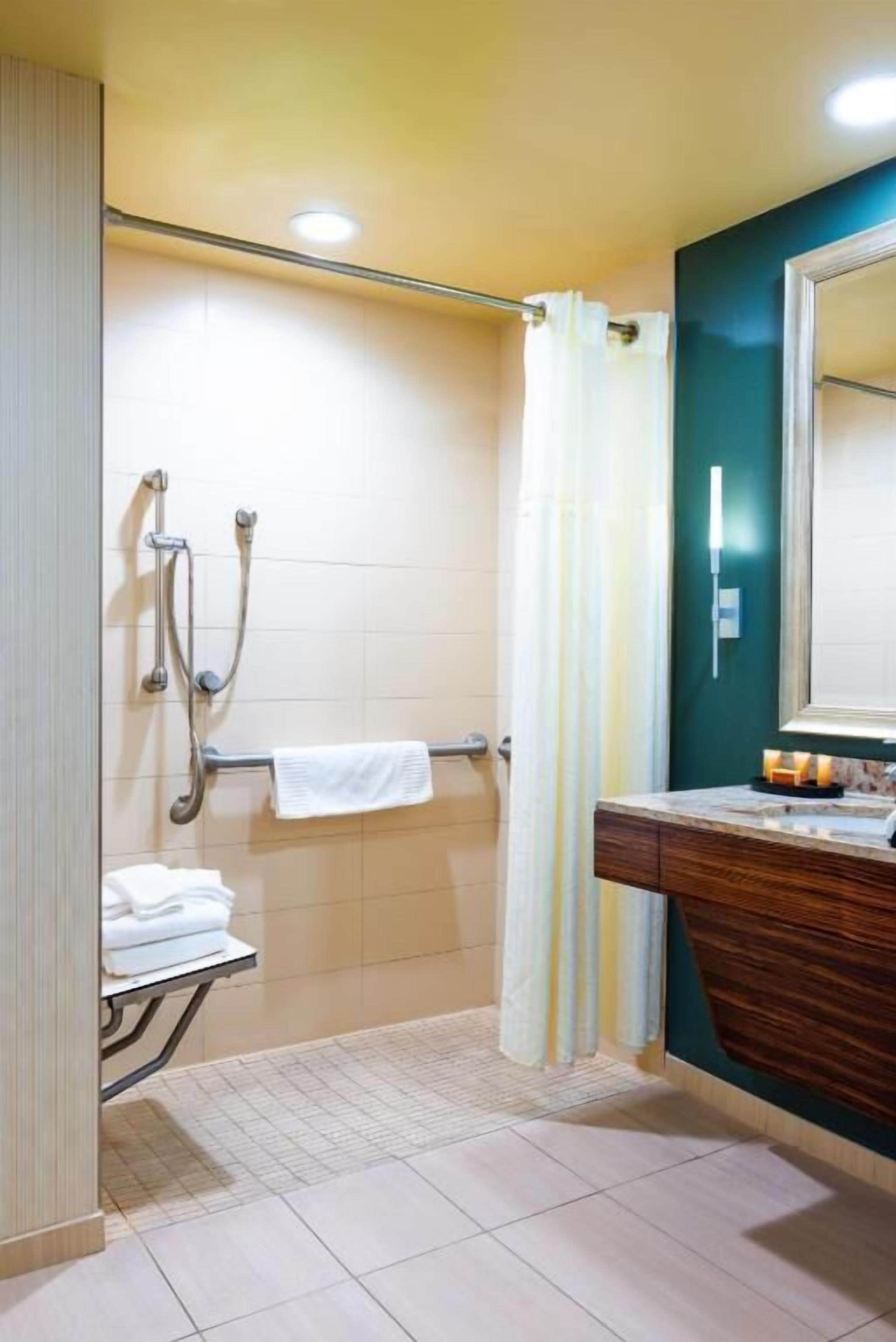 A bathroom with a shower, a towel rack, a mirror, and a vanity with a sink.