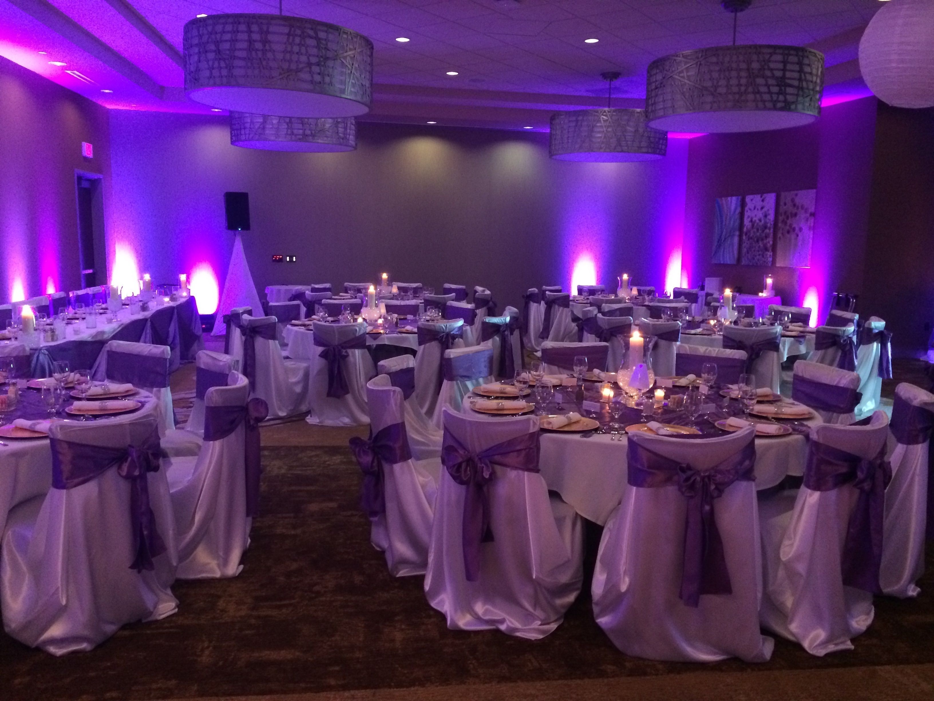 Un salón de banquetes con mesas redondas, iluminación morada y candelabros.