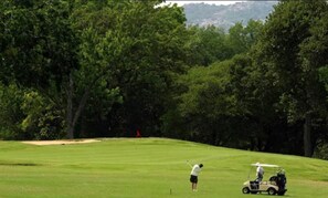 A golf course with a golfer and a golf cart.