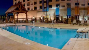 Piscina con sillas de descanso y un área de estar techada, rodeada por un edificio con múltiples ventanas y balcones.