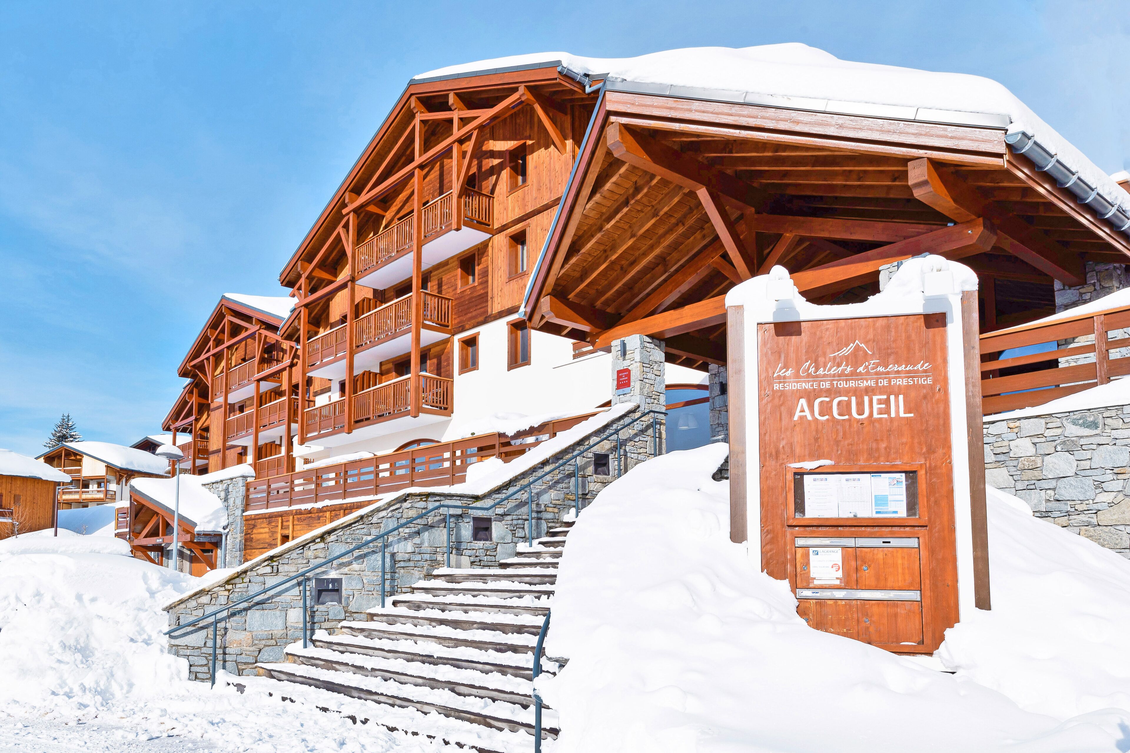 A wooden chalet-style building with multiple balconies and a stone staircase leading to the entrance.
