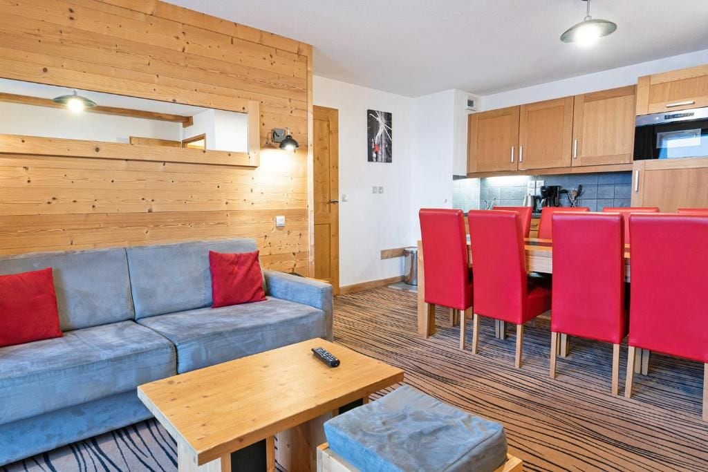 Un salon moderne avec un canapé, une table basse et un coin repas avec des chaises rouges.