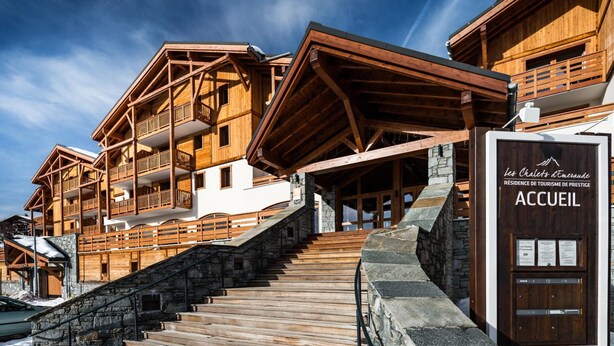 Un edificio de estilo chalé de madera con varios balcones y una escalera de piedra que conduce a la entrada.