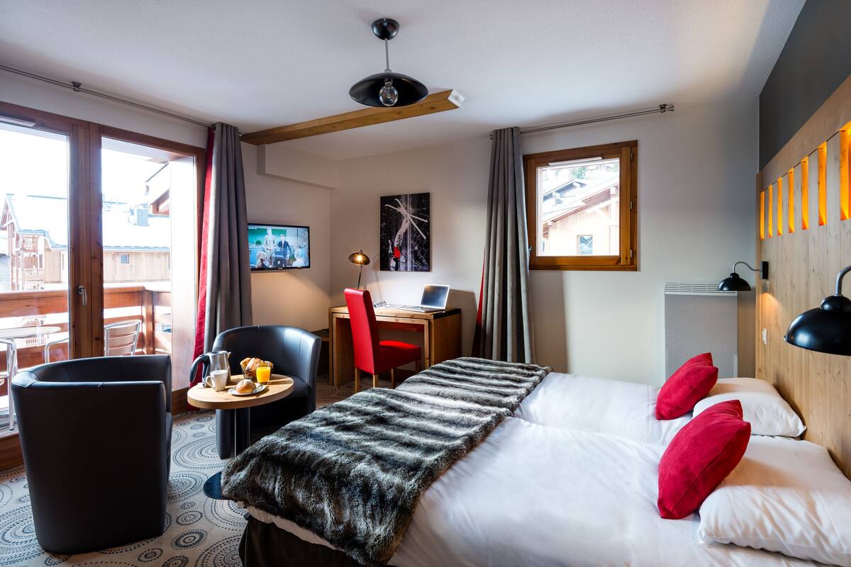 Una habitación de hotel con una cama, un escritorio con una computadora portátil, una silla, una pequeña mesa con alimentos para el desayuno y vistas al exterior.