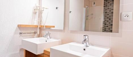 A bathroom with two sinks, a mirror, and a shower.
