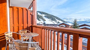 Un balcón de madera con una mesa y sillas, con vistas a un paisaje montañoso nevado.