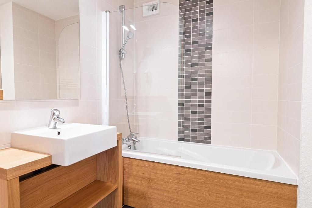 Une salle de bain moderne avec un lavabo blanc, un meuble-lavabo en bois et une douche séparée par une paroi de verre.