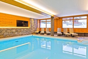 Ein Hallenbad mit Liegestühlen und einer Steinwand.