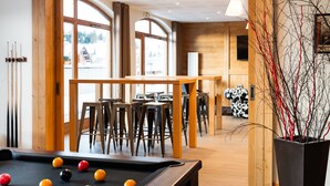 Una mesa de billar con bolas, taburetes de madera y una zona de bar con sillas.