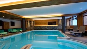 Una piscina con sillas de descanso y un muro de piedra de fondo.