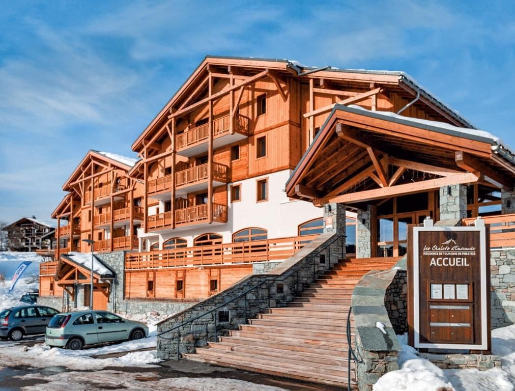A wooden multi-story building with balconies and a stone staircase leading to the entrance.