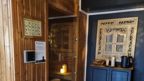 Una sauna de madera con puerta, una mesita con hervidor y un cartel en la pared.