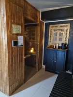 Una sauna de madera con puerta, una mesita con hervidor y un cartel en la pared.
