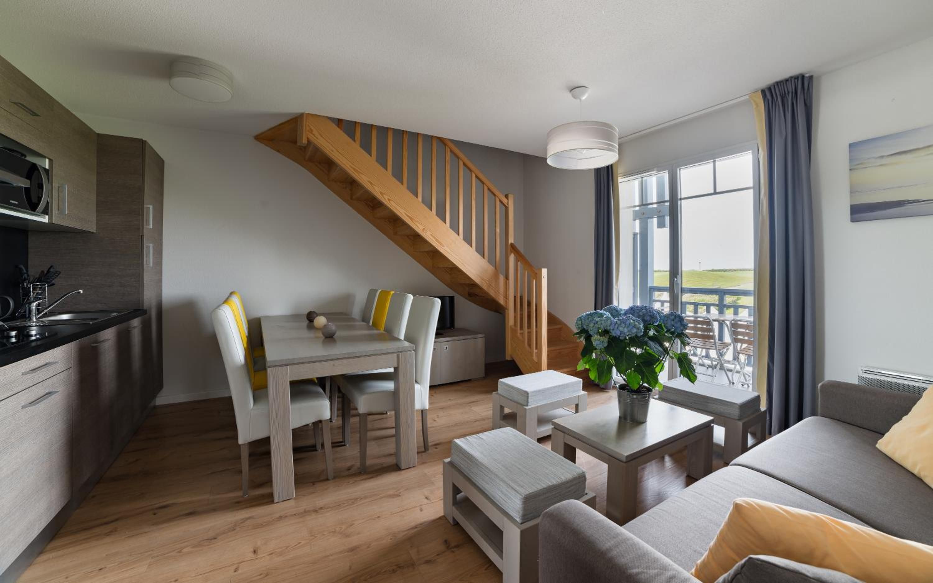 A modern living room with a wooden staircase, a dining area, and a view of the outdoors.