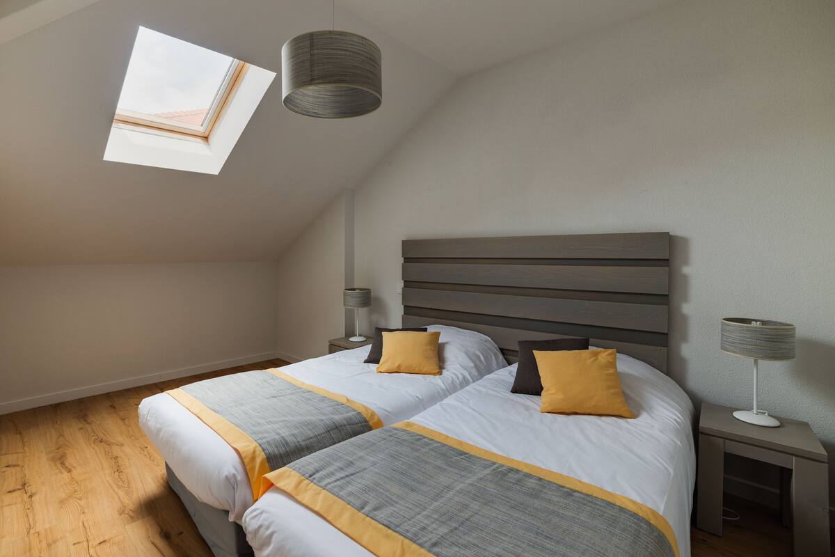 Slaapkamer met schuine kap, dakraam, bed met twee kussens, bedlampen en nachtkastje.