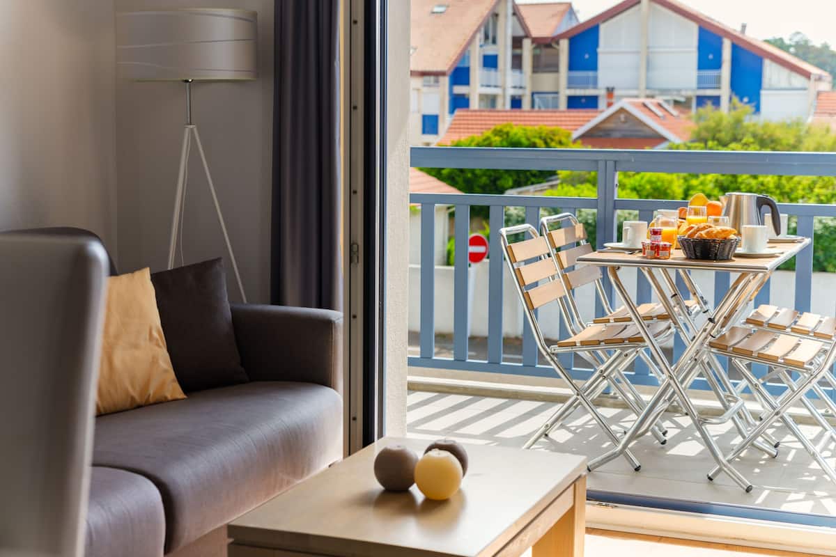 Een moderne woonkamer met een grijze bank, een bijzettafeltje met decoratieve objecten, en een balkon met een eethoek.