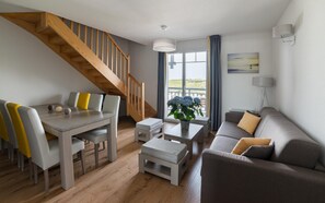 Un salon moderne avec un escalier en bois, un coin repas avec des chaises et une table, un canapé et une grande fenêtre offrant une vue dégagée.
