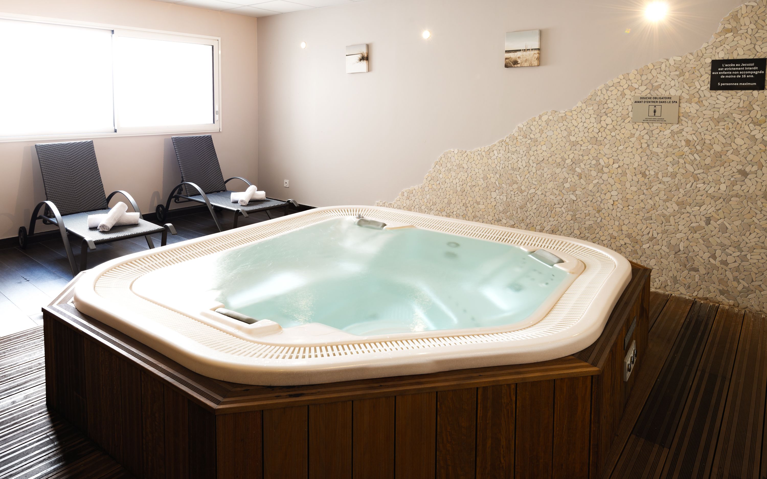 A spa area with a hot tub, two chairs, and a pebble wall.