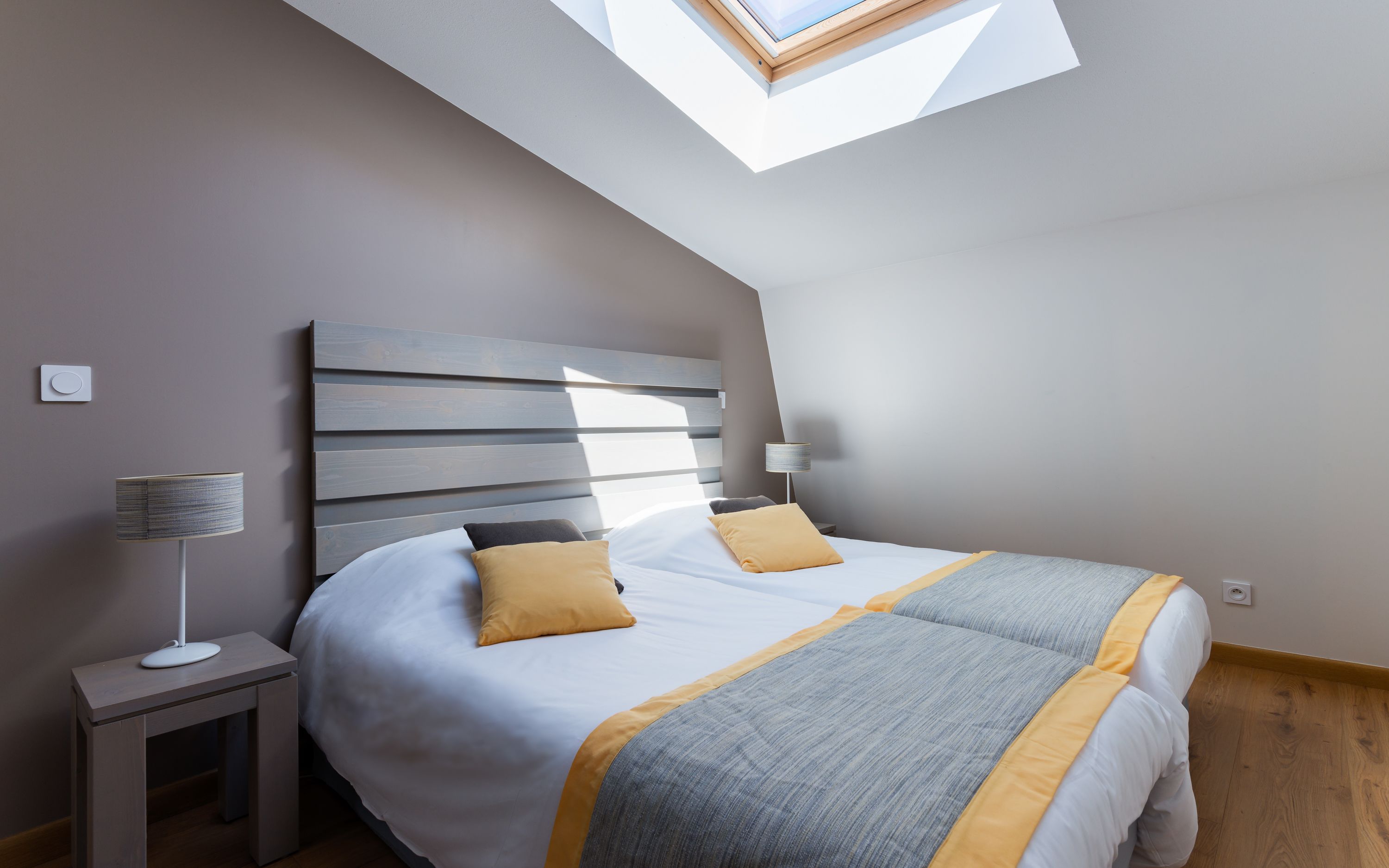 Een slaapkamer met dakraam, een bed met twee kussens, een bedlampje en een nachtkastje.