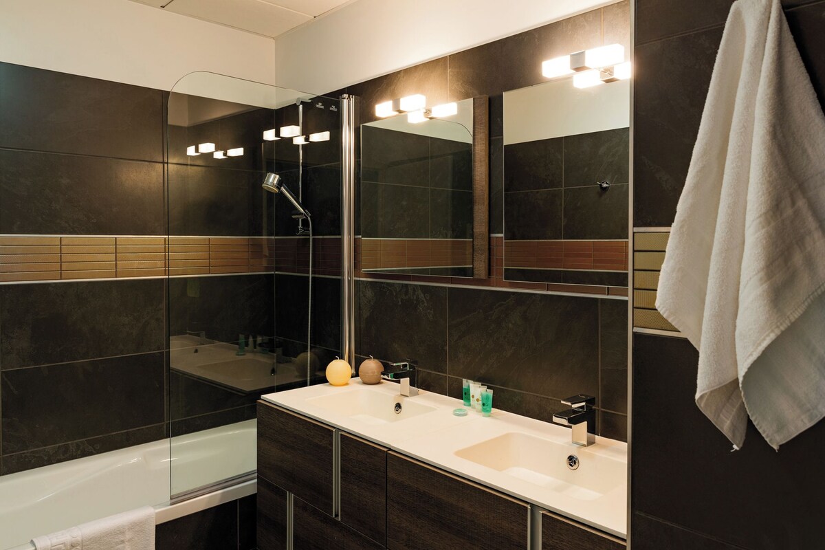 Un baño moderno con un espejo grande, una bañera, un lavabo y una ducha.