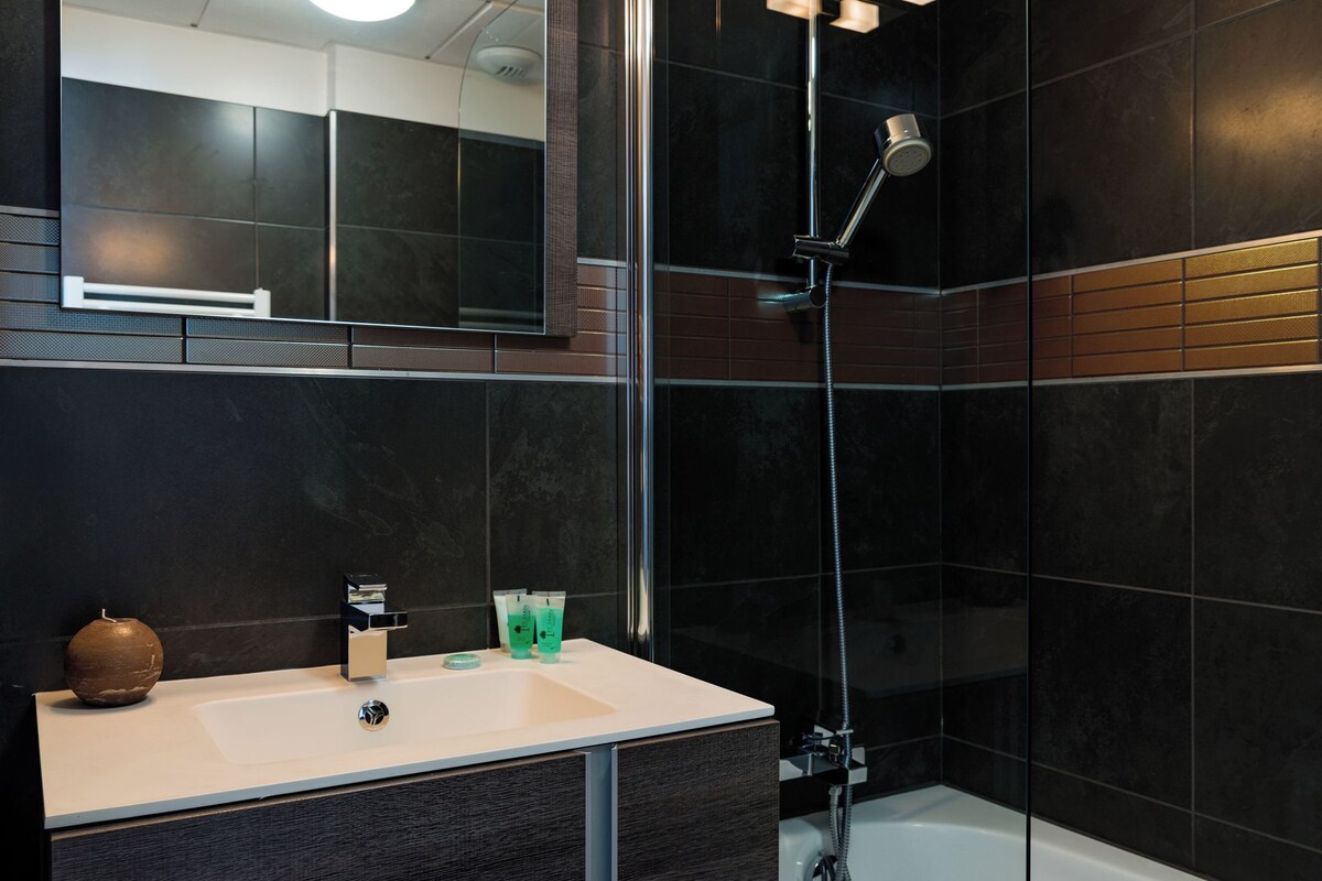 A modern bathroom with a large mirror, a sink, and a shower.