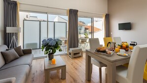 Ein modernes Hotelzimmer mit Balkon, einer Essecke mit Frühstück und einem an der Wand befestigten Fernseher.