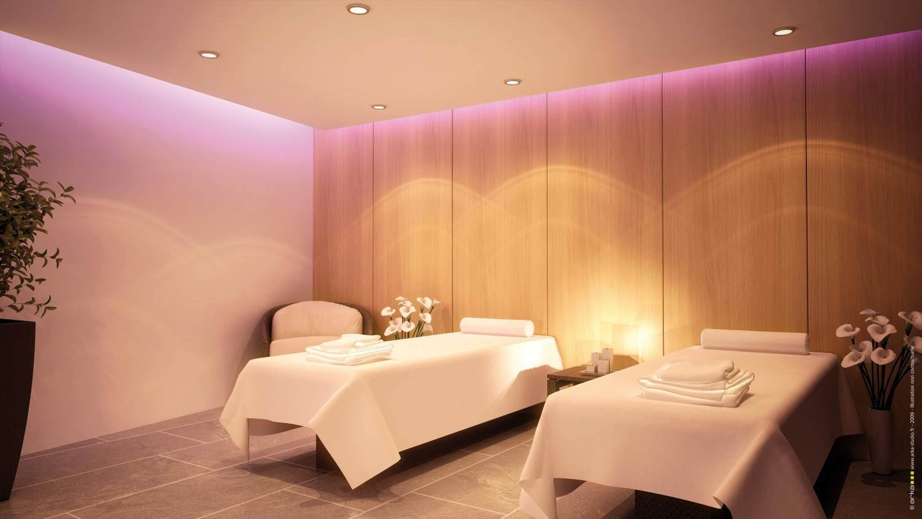 Een moderne spa-ruimte met twee massagetafels, elk met een handdoek en een klein tafeltje met een lamp.
