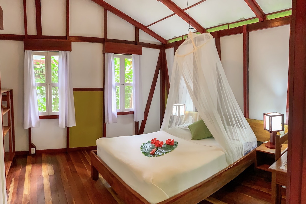 A room with a bed, a nightstand, a lamp, and a window with a view of greenery.