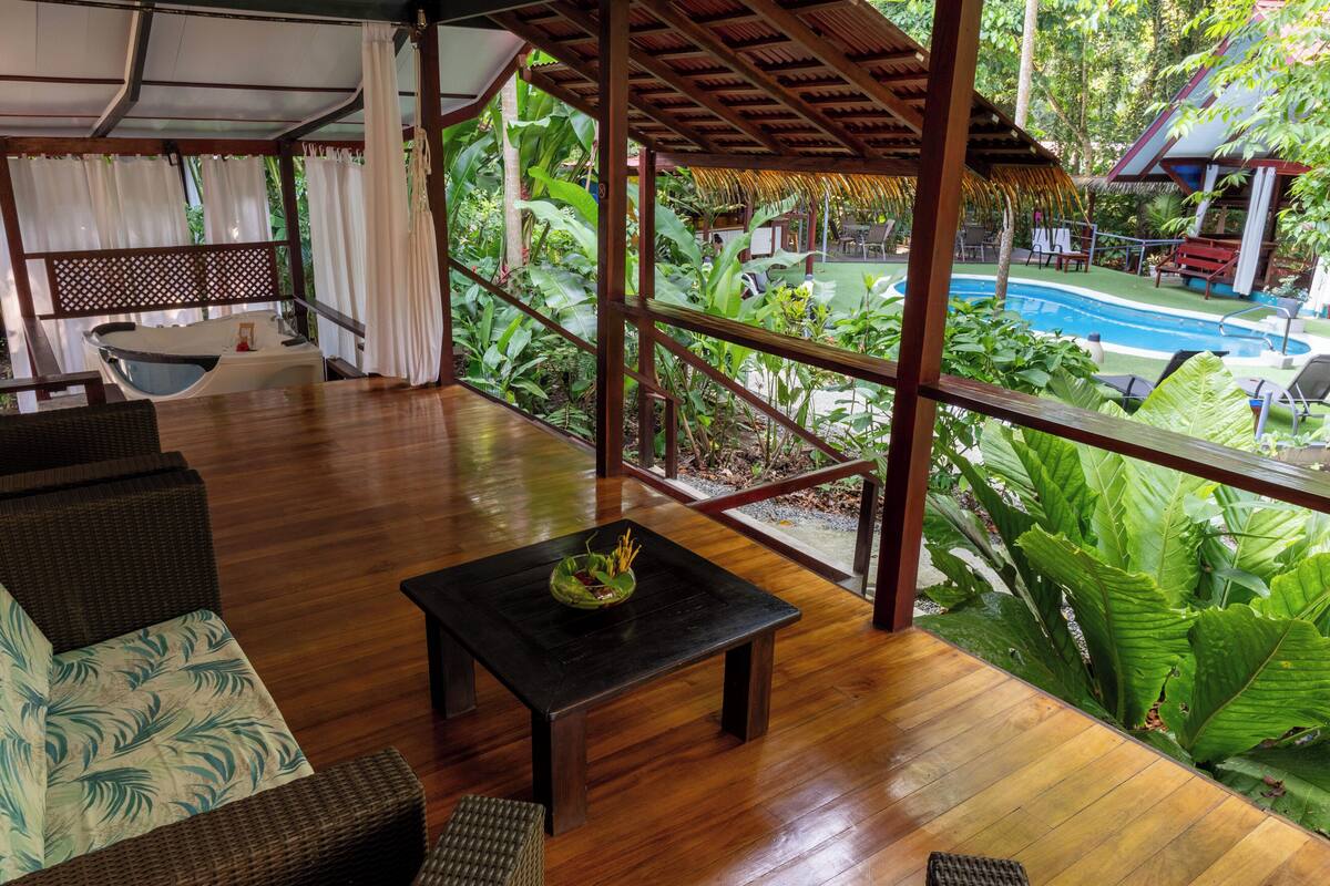 A wooden deck with a pool, wicker furniture, and tropical plants.