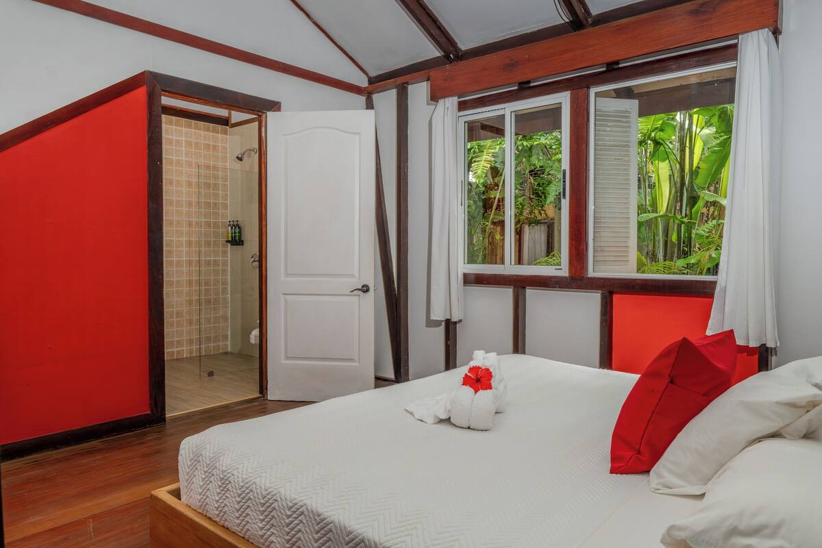 A hotel room with a bed, a shower, and a view of greenery outside.