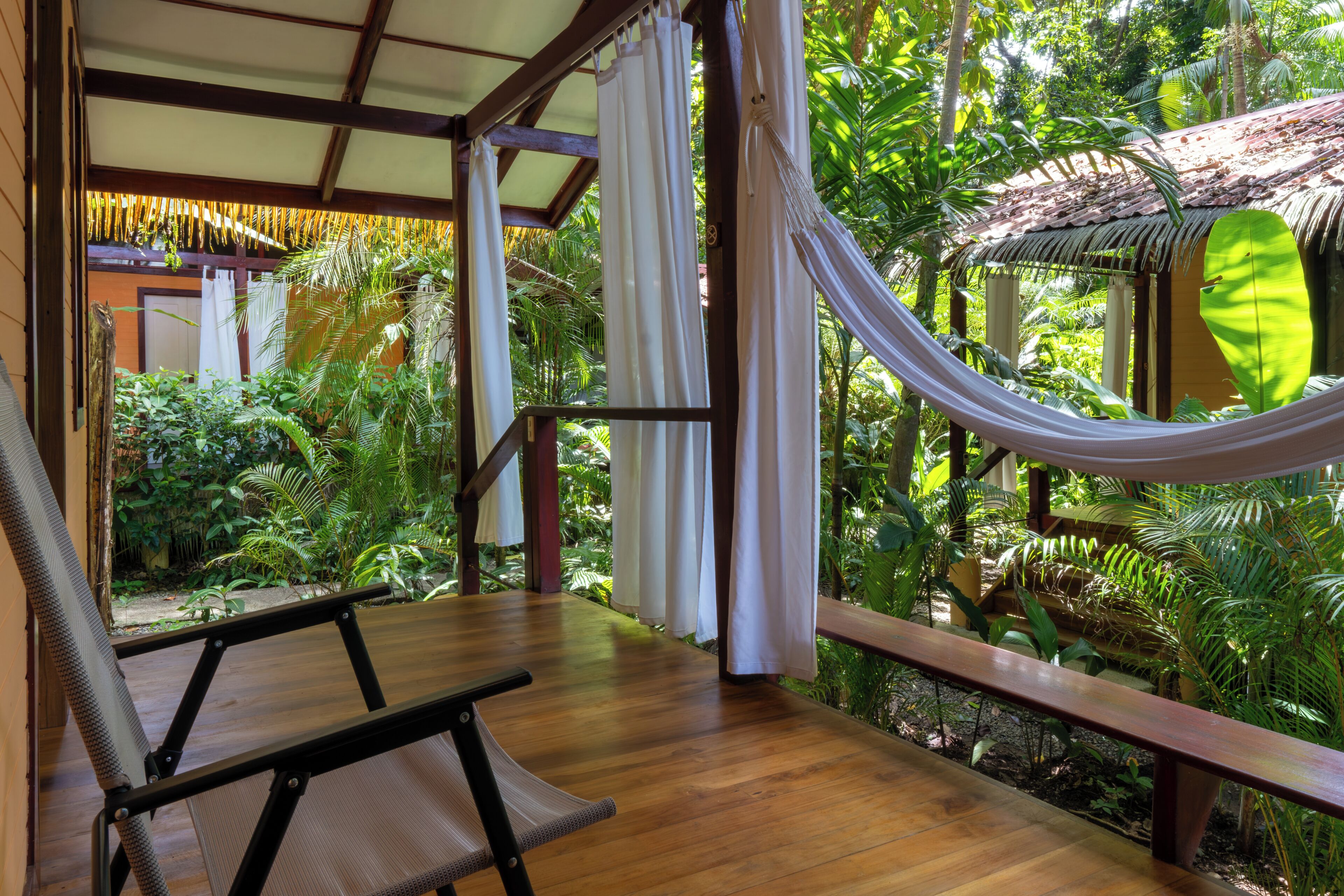 A wooden deck with a hammock, a chair, and a view of lush greenery.