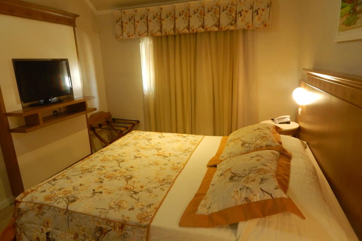 A hotel room with a bed, a television, a chair, a bedside table with a lamp, and a telephone.