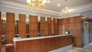 A reception desk with a wooden finish, a chandelier, and a mirror wall. - Life Hotel Infinity (Gramado)