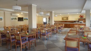 A spacious dining area with multiple tables and chairs, a kitchen in the background, and a television on the wall. - Life Hotel Infinity (Gramado)