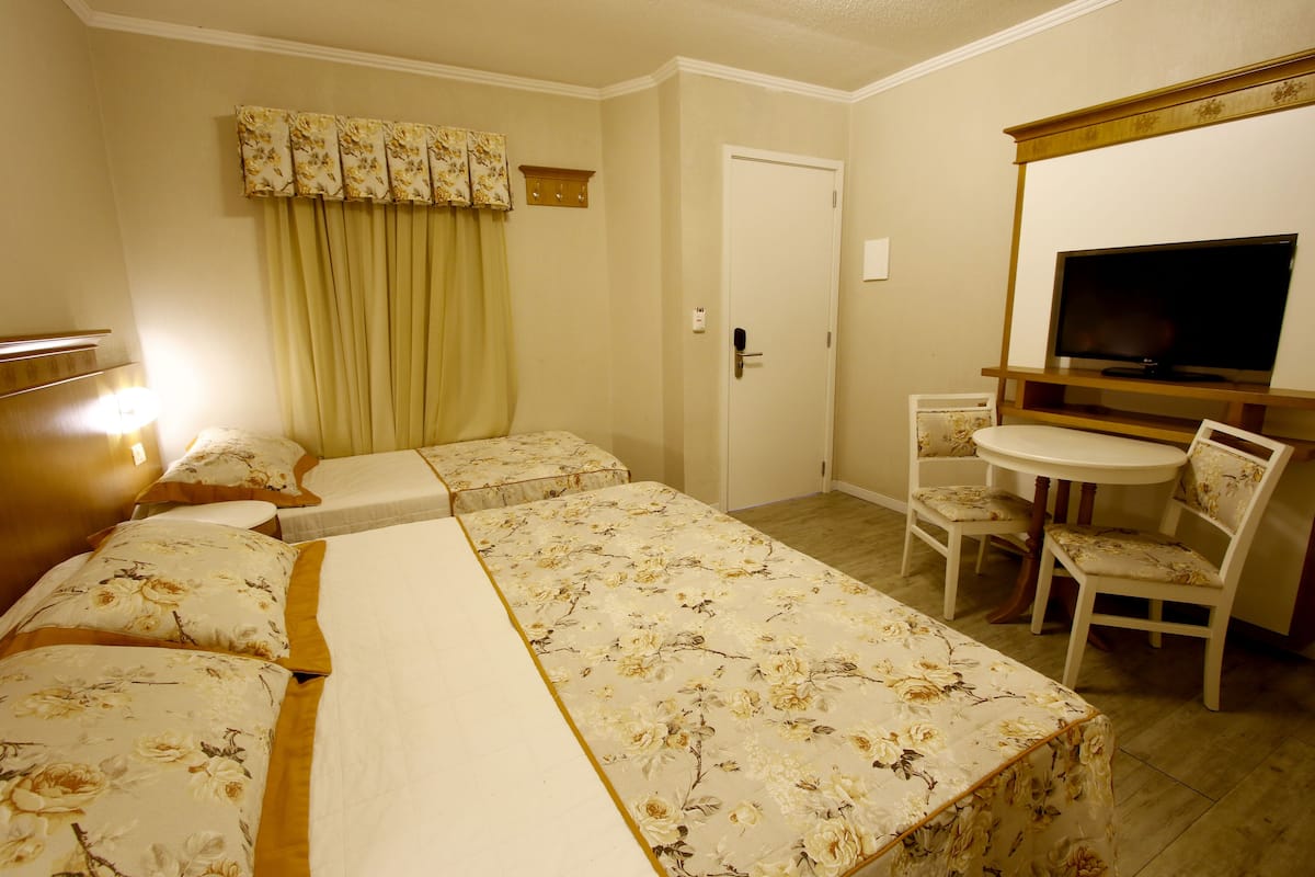 A hotel room with two beds, a small dining table, a TV, and a door.