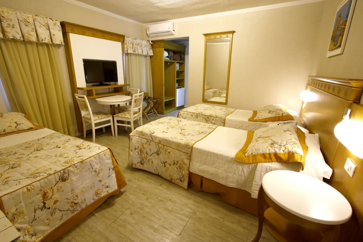 A hotel room with two beds, a desk, a chair, a television, a mirror, and an air conditioning unit.