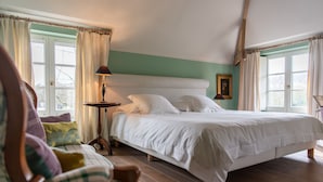 Quarto com uma cama grande, piso de madeira, mesa de cabeceira e uma cadeira.