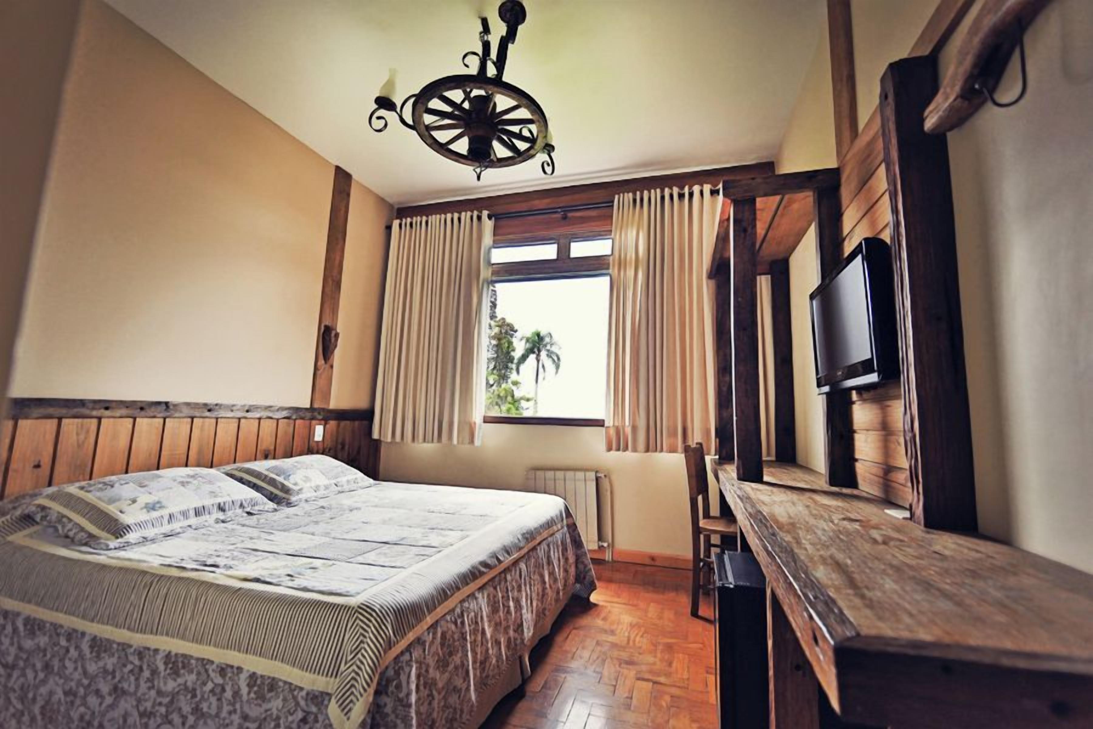 Une chambre à coucher avec un lit, un bureau en bois, une télévision et une fenêtre avec des rideaux.