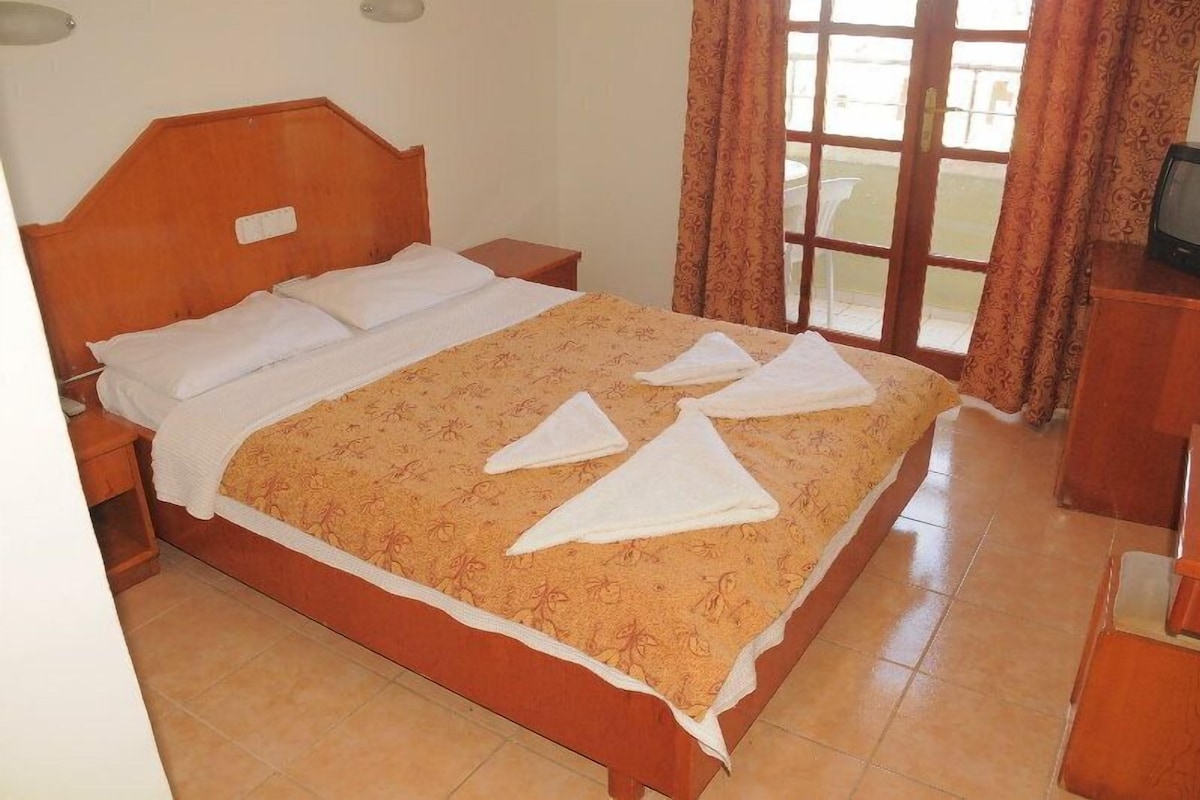 A neatly made bed with a patterned bedspread, a wooden headboard, and a nightstand with a television.