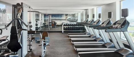 Ein Fitnessstudio mit Laufbändern, Kraftgeräten und Kurzhanteln.