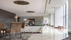 Un moderno vestíbulo de hotel con barandilla de vidrio, zona de estar e iluminación contemporánea.