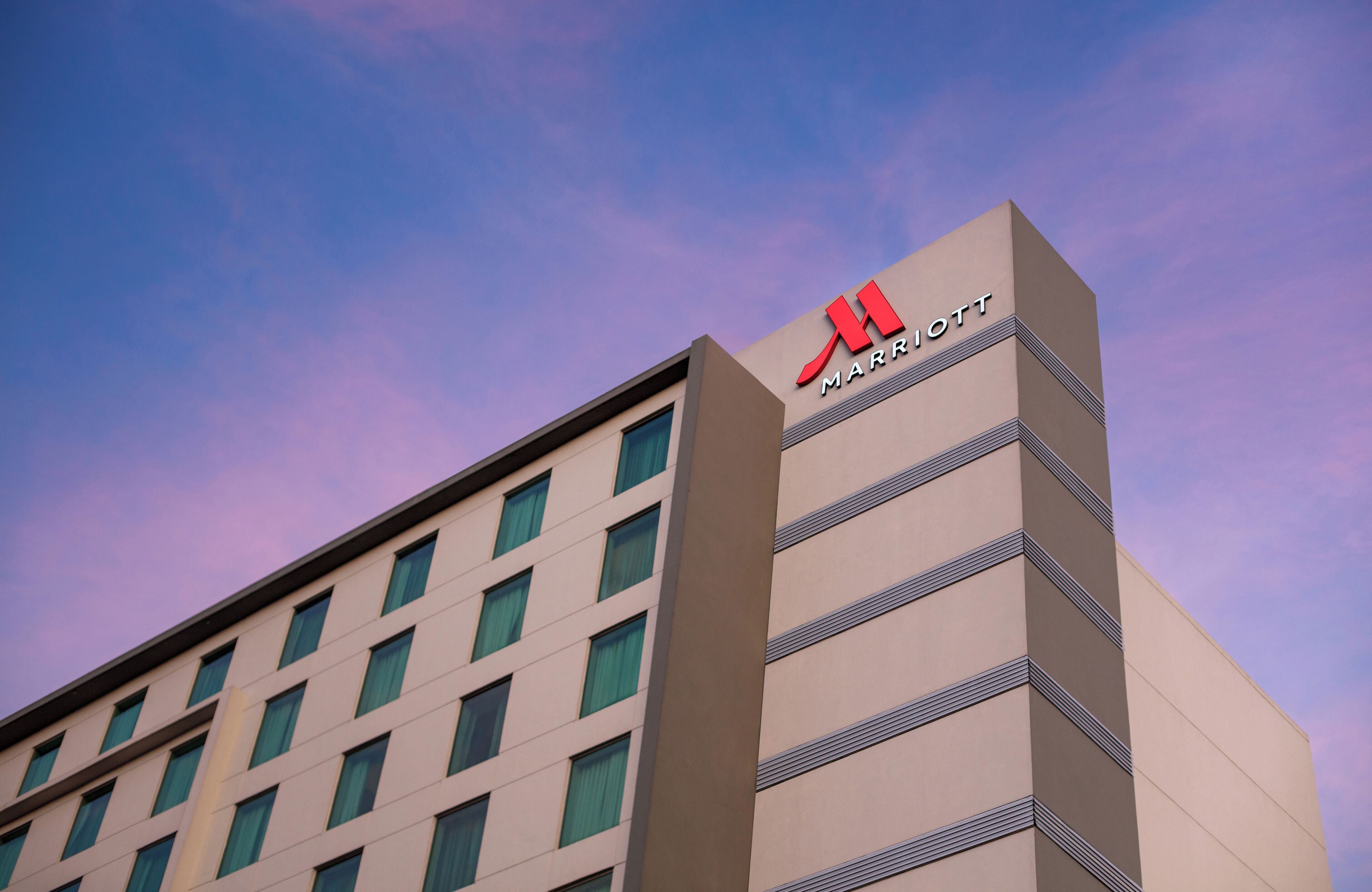 Een modern hotelgebouw met een opvallend rood logo bovenaan.