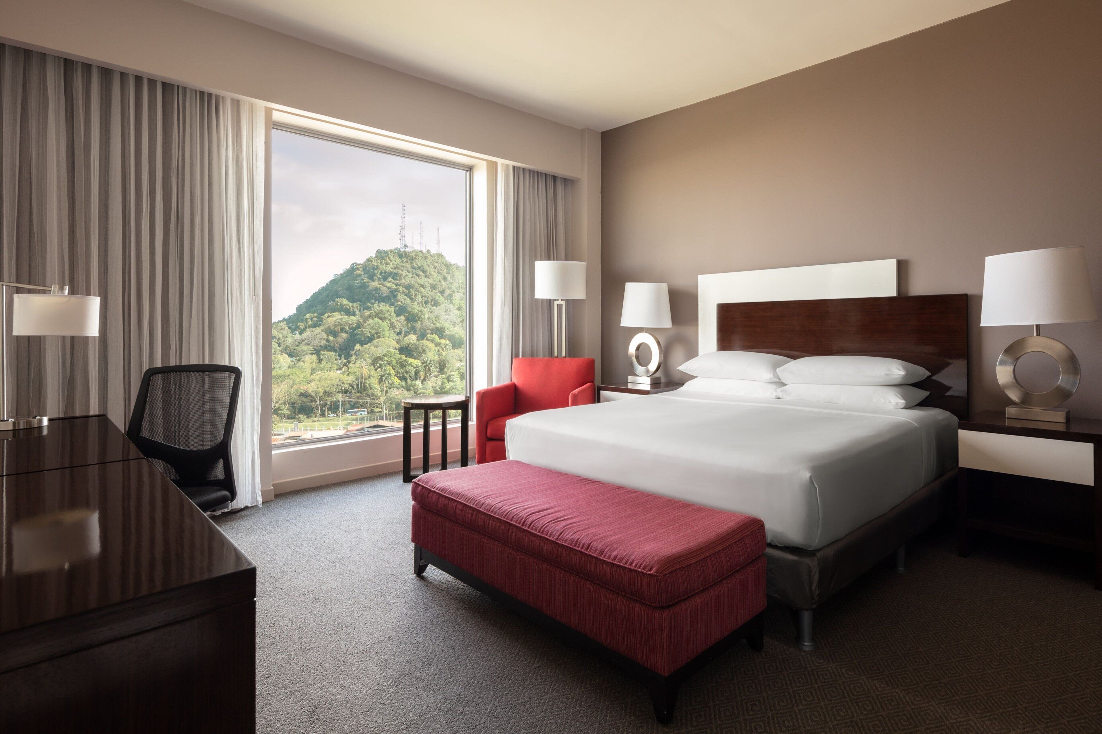 Habitación de hotel con una cama grande, un escritorio, una silla y vistas a la montaña.