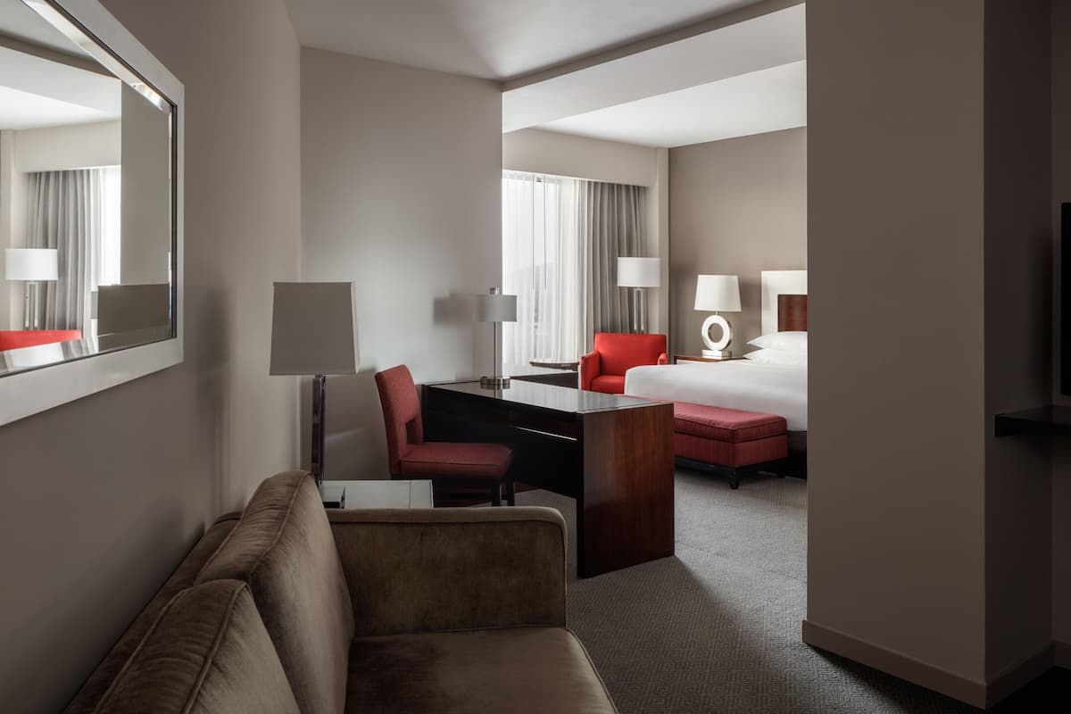 A hotel room with a sofa, a desk, a red chair, a bed, and a large mirror.