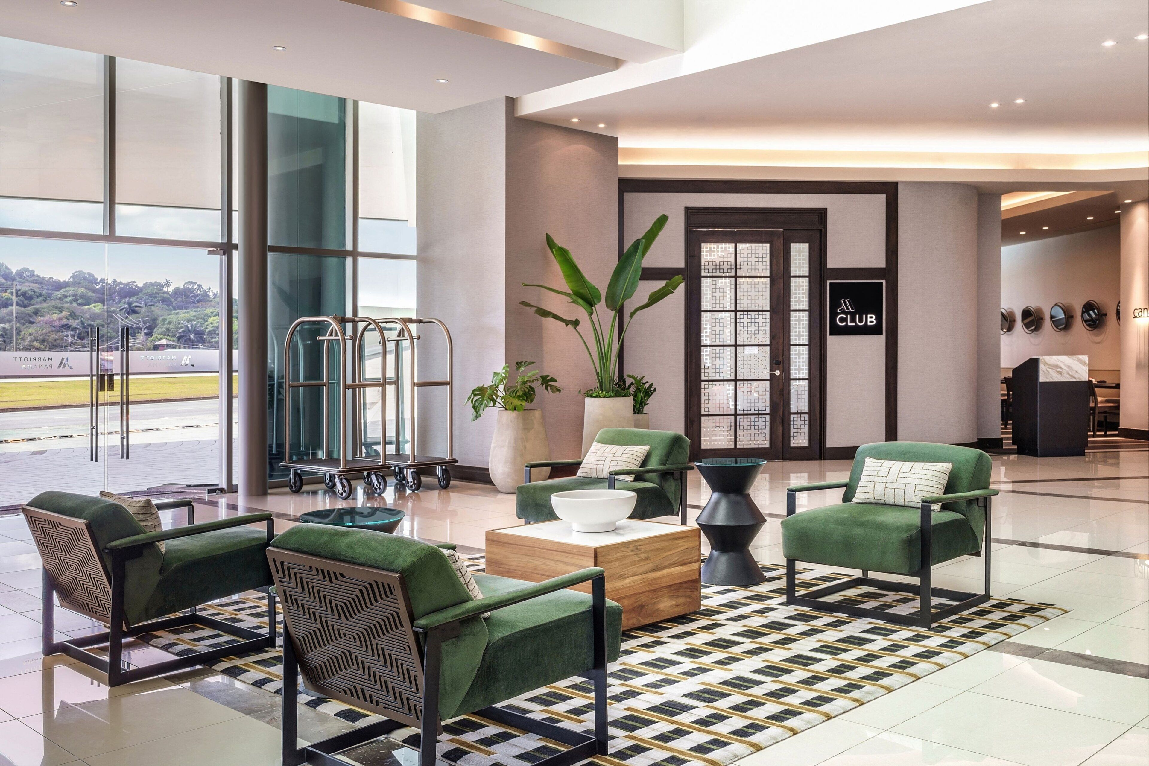 A modern lobby with green armchairs, a coffee table, and large windows offering a view of the airport.