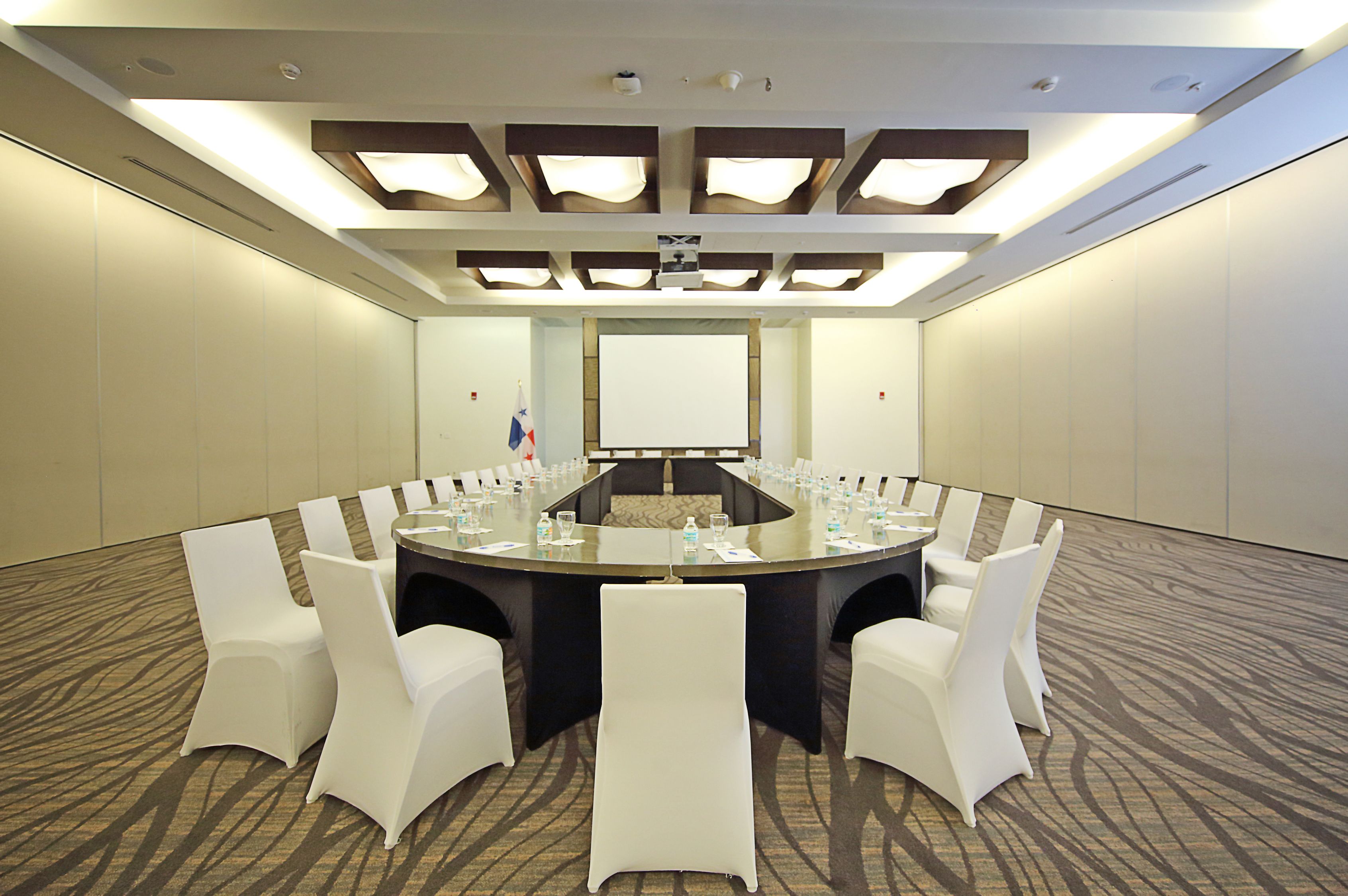 Une salle de conférence équipée d’une table ronde, de chaises blanches et d’un écran de projection.