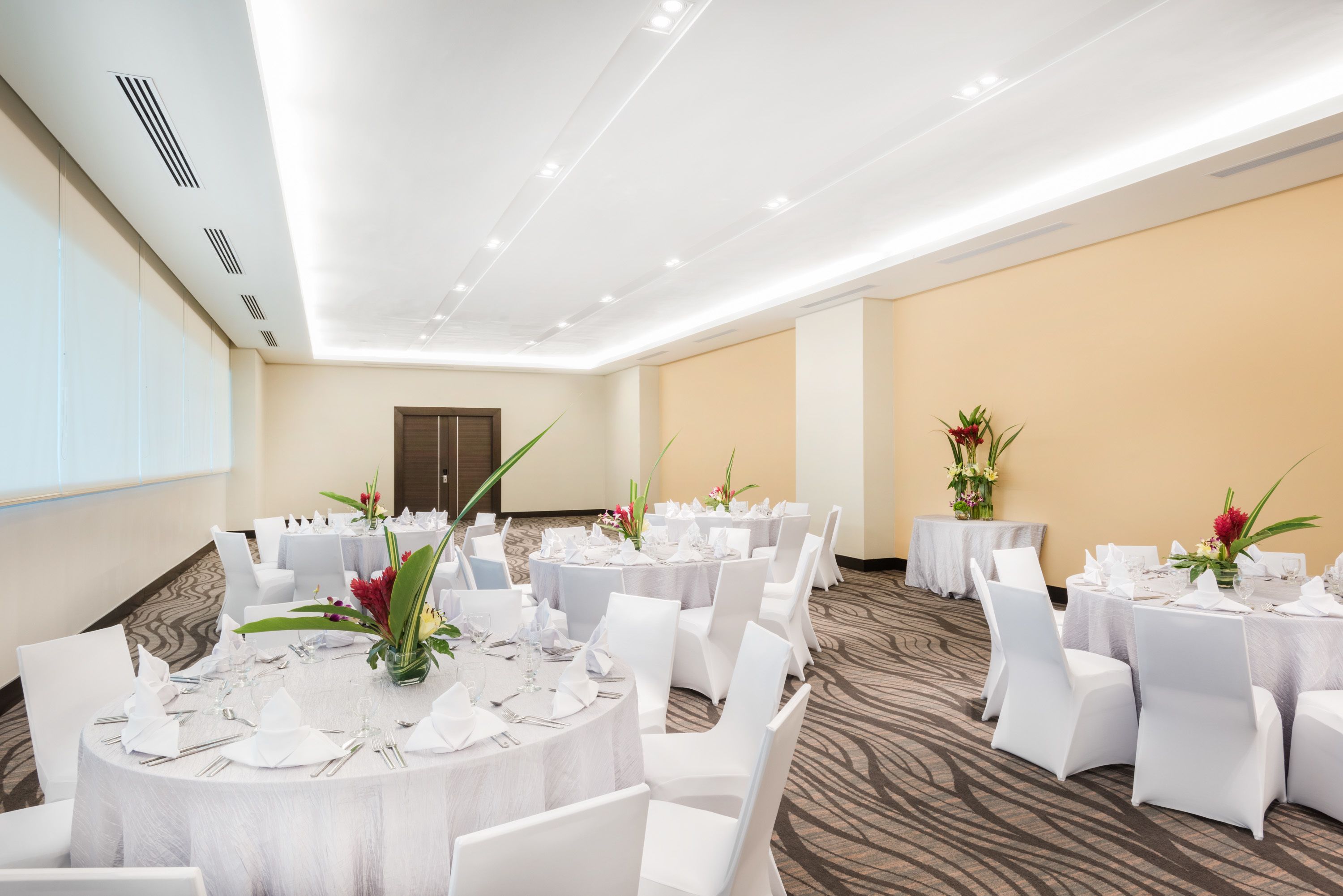 A conference room with round tables, white chairs, and floral centerpieces.