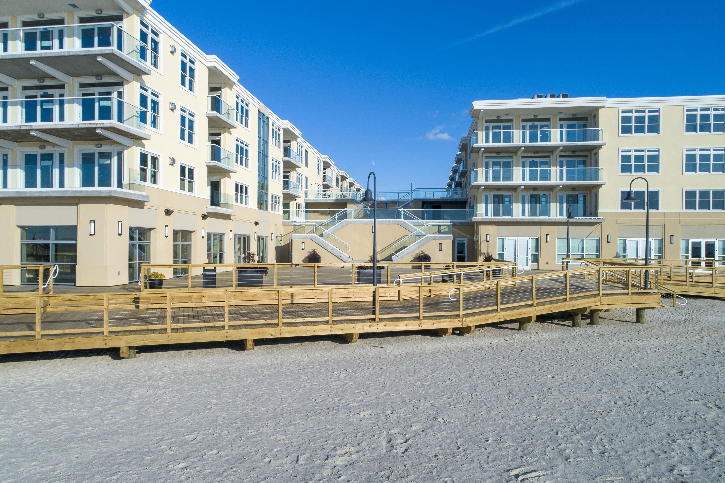 Ein Strandhotel mit mehreren Balkonen, einer Holzpromenade und blauem Himmel.